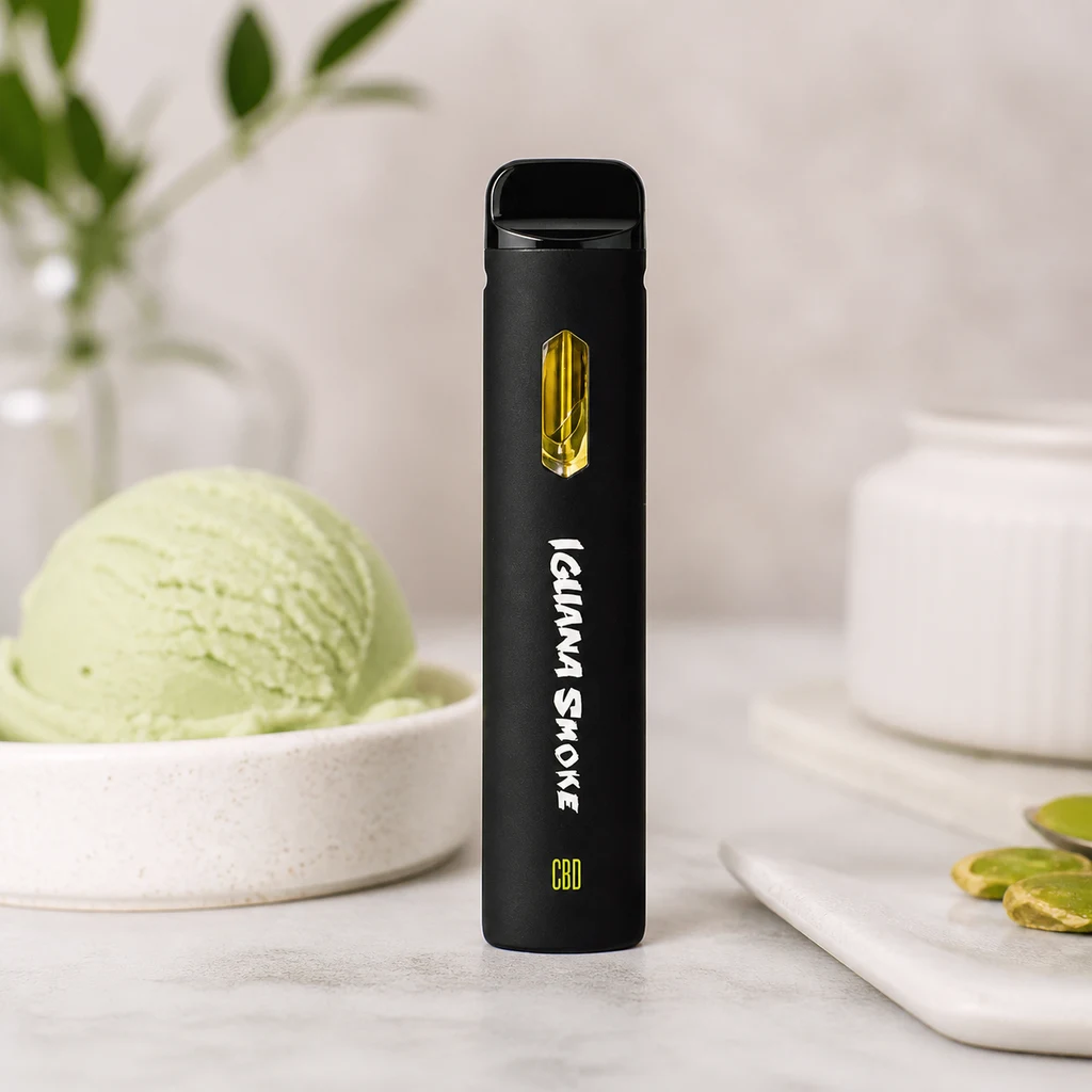 Pod negro Iguana Smoke en posición vertical, con ventana amarilla e inscripción CBD, junto a helado verde y pistachos.