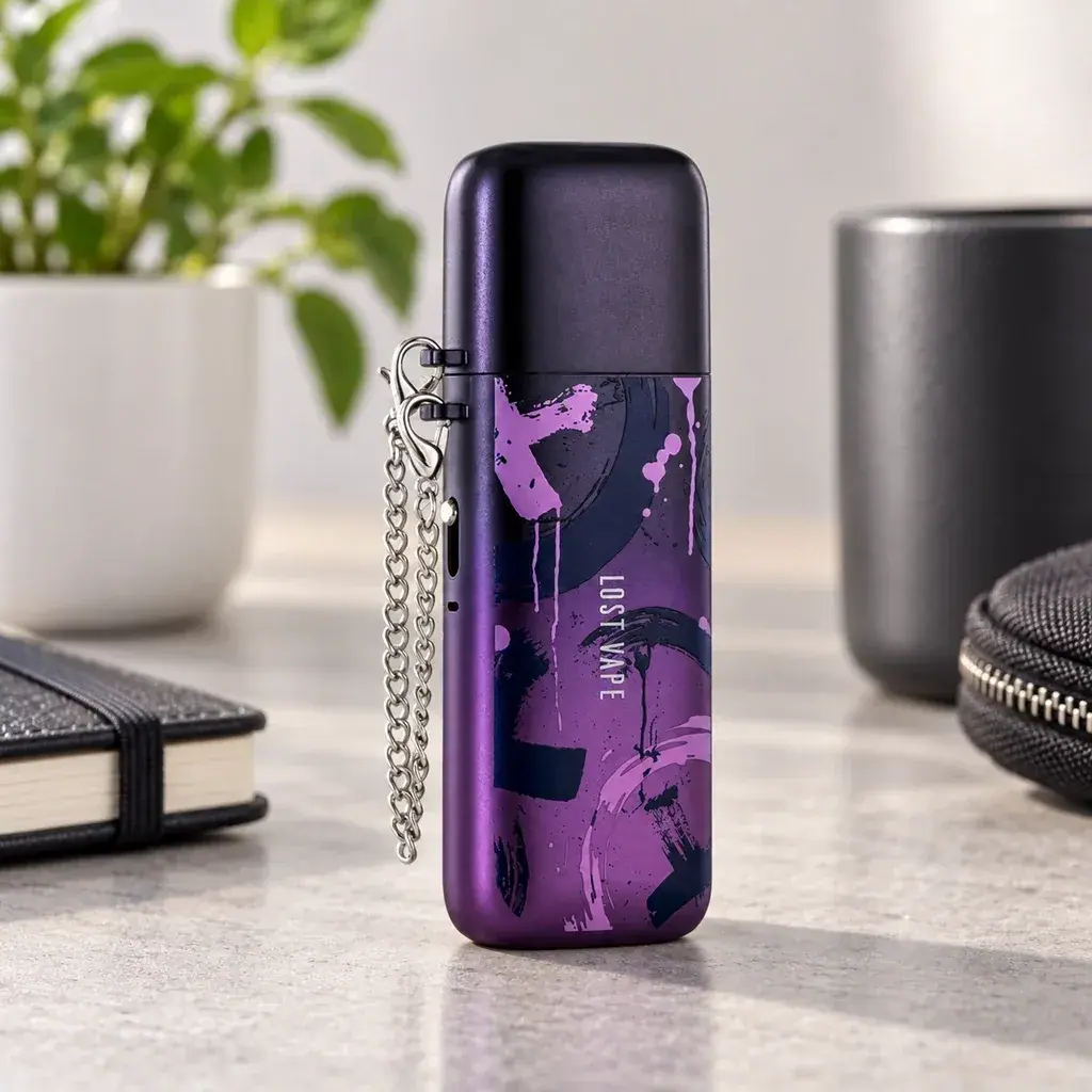 Vaper Lost Vape morado con estampado abstracto, tapa oscura y cadena plateada, de pie sobre una mesa junto a objetos desenfocados.