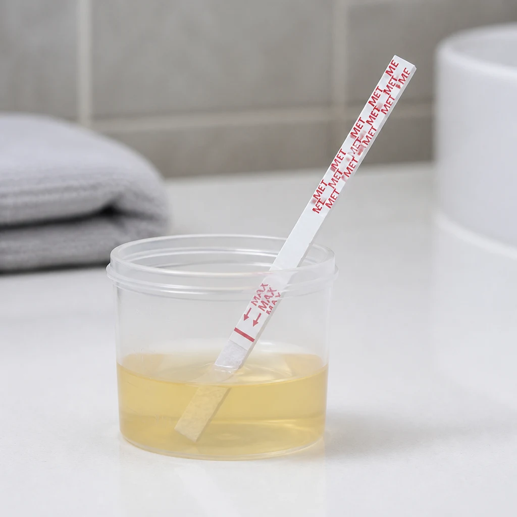Tira de prueba con las inscripciones MET y MAX introducida en un recipiente transparente con líquido amarillo sobre una encimera.