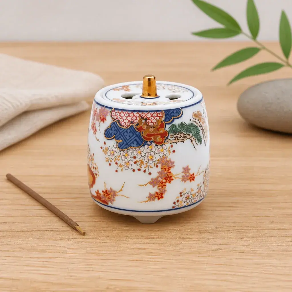 Quemador de incienso Shunjyumon con decoración floral multicolor y tapa perforada, sobre una mesa de madera junto a una varilla.