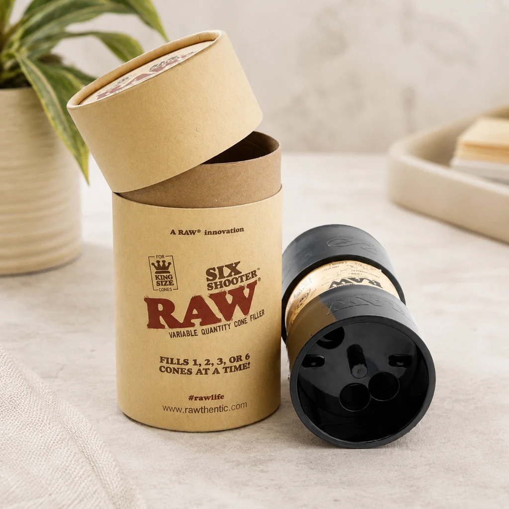 Raw Six Shooter King Size negro, tumbado con los orificios de su base a la vista, junto a su envase cilíndrico abierto. Raw Six Shooter King Size negro, tumbado con los orificios de su base a la vista, junto a su envase cilíndrico abierto.