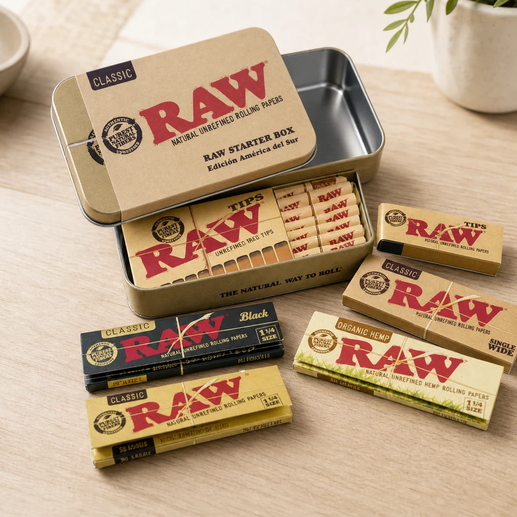 Caja metálica RAW Starter Box abierta sobre una mesa, con papeles y tips; alrededor se muestran distintos formatos RAW Classic, Black y Organic Hemp. Caja metálica RAW Starter Box abierta sobre una mesa, con papeles y tips; alrededor se muestran distintos formatos RAW Classic, Black y Organic Hemp.