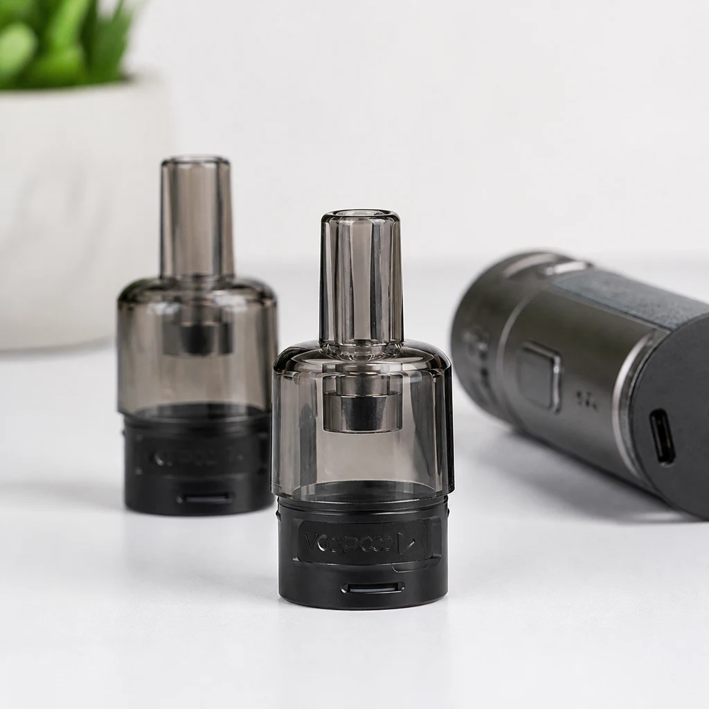 Cartuchos Voopoo ITO transparentes ahumados, con boquilla alargada y base negra, junto a un dispositivo tumbado.