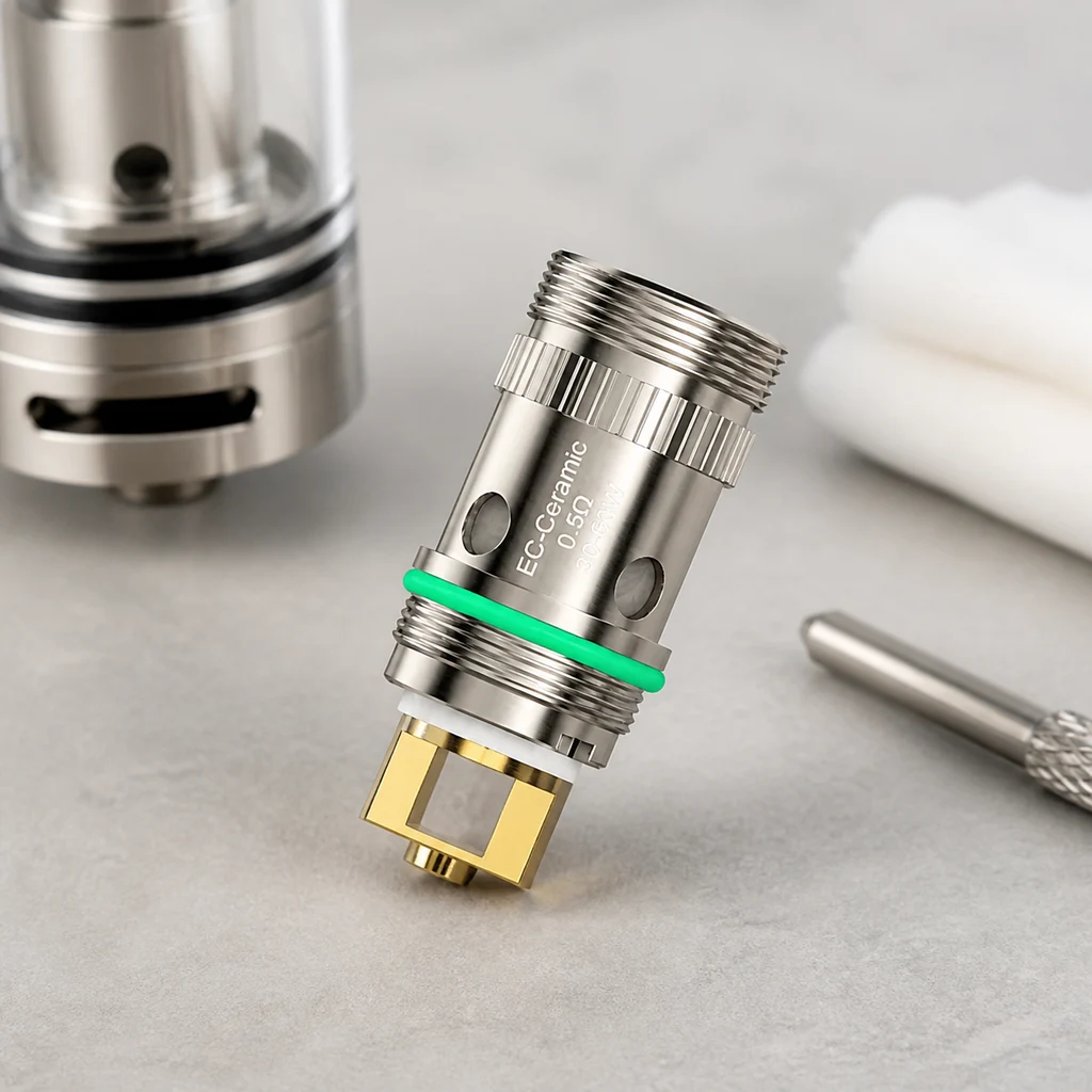 Resistencia Eleaf EC Ceramic de 0,5 Ω inclinada, con roscas, junta verde y contacto dorado, junto a un depósito y algodón.