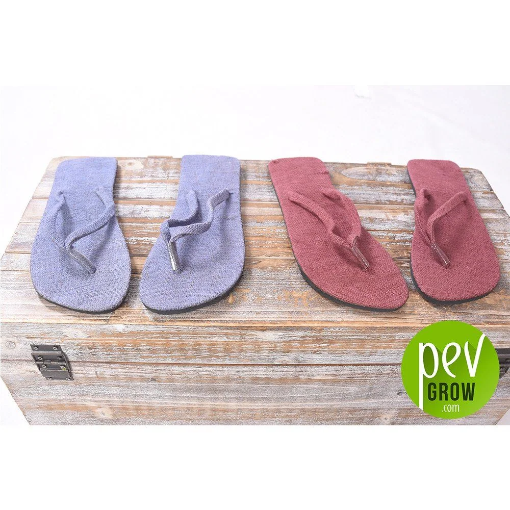 Chanclas de tira entre los dedos en tonos lila y granate, colocadas sobre un baúl de madera con el logotipo de Pevgrow.