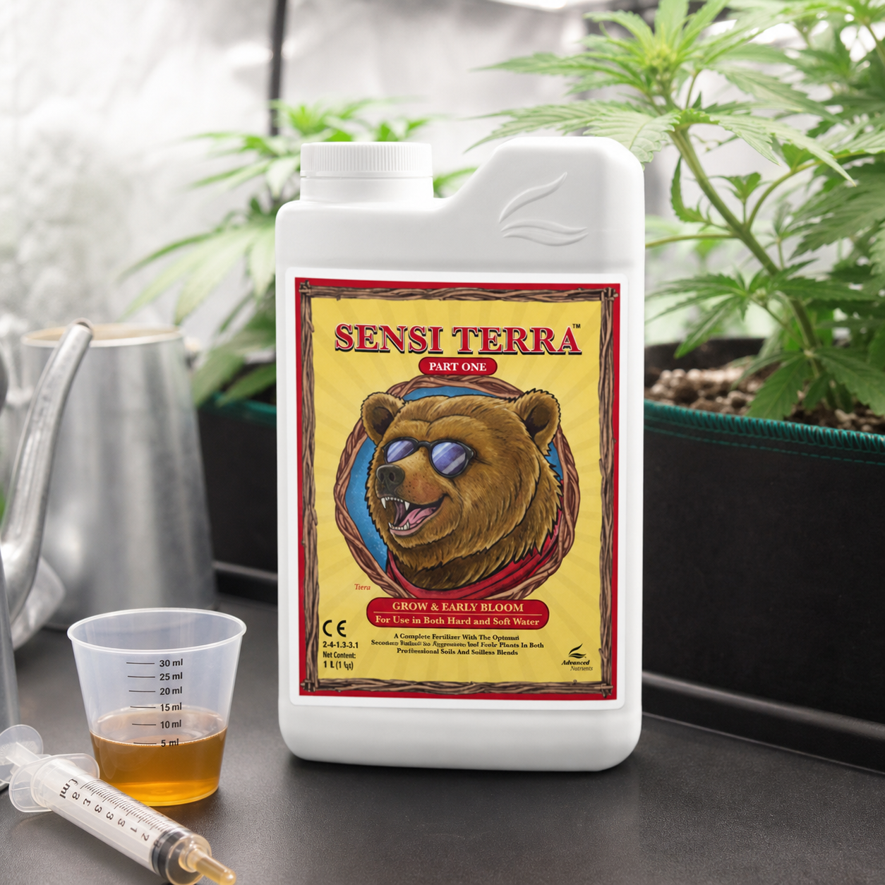 Envase de Sensi Terra Part 1 con un oso con gafas en la etiqueta, junto a un vaso dosificador y una jeringa, con plantas al fondo.