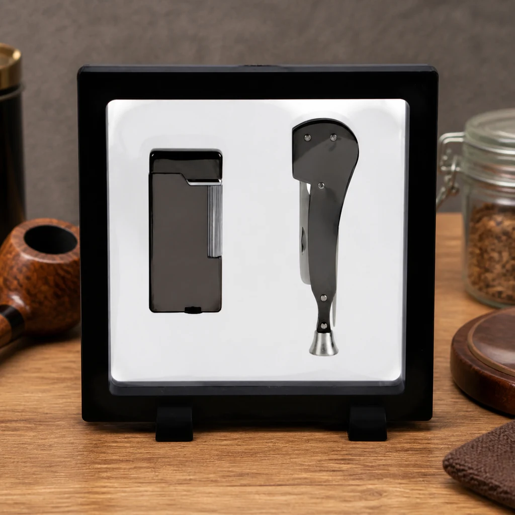 Set Jean Claude con mechero rectangular y apisonador plegable gris oscuro, expuesto en un marco negro junto a una pipa y un tarro.