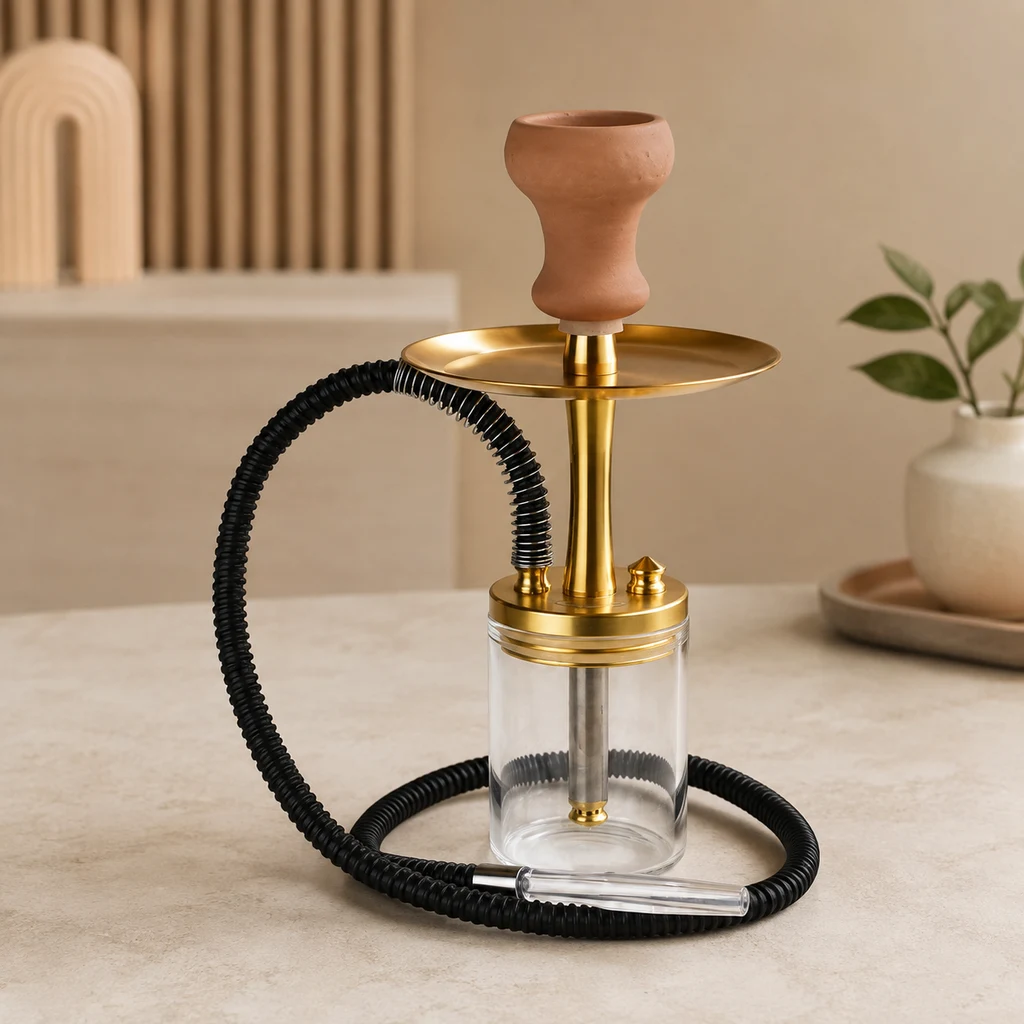 Cachimba Al Malik Deroua con cuerpo dorado, base transparente, cazoleta de tono terracota y manguera negra sobre una mesa.