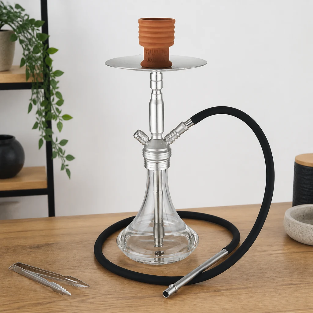 Cachimba Al Malik Marrakech con base transparente, cuerpo plateado, cazoleta marrón y manguera negra, sobre una mesa con pinzas.