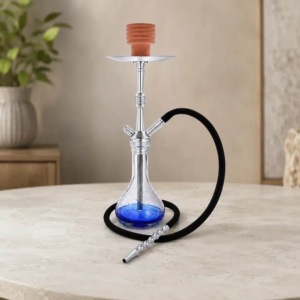 Cachimba Al Malik Oulmes con cuerpo plateado, base transparente con fondo azul, cazoleta terracota y manguera negra sobre una mesa.