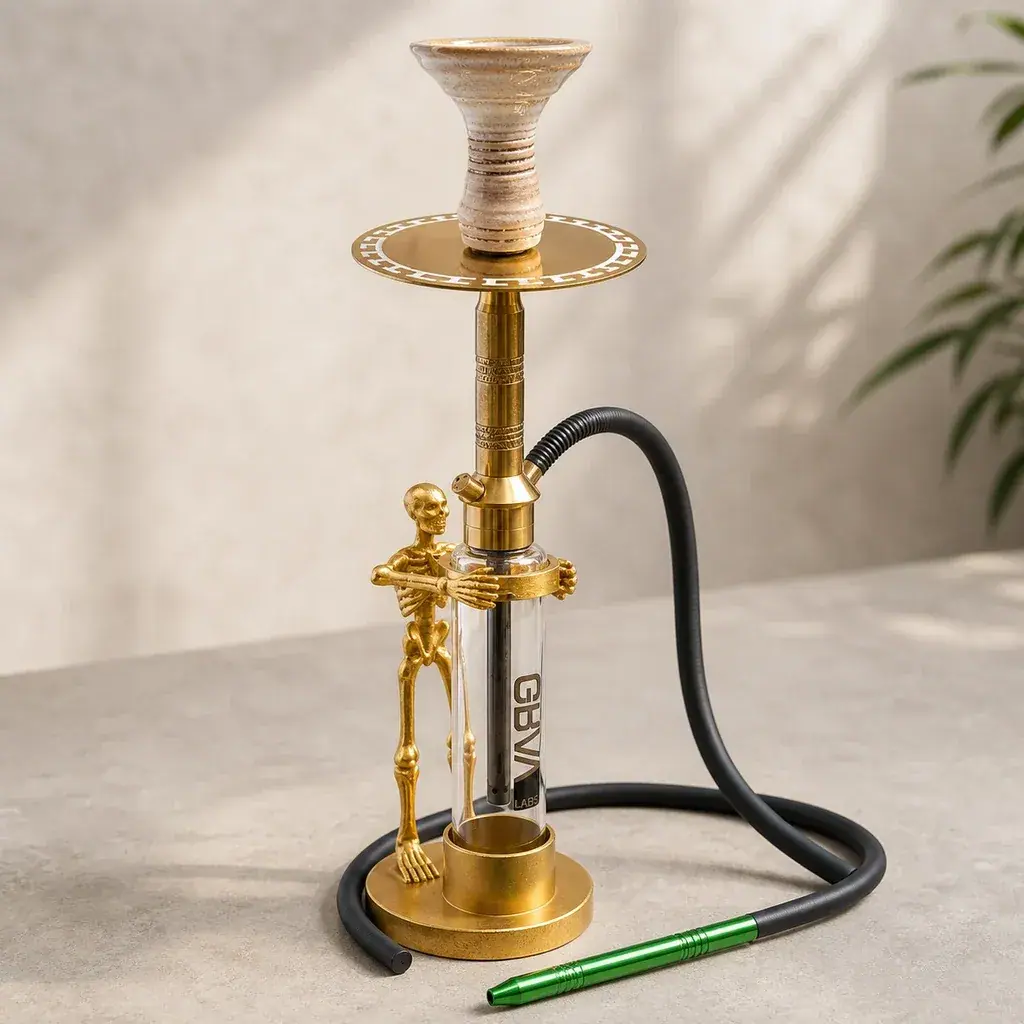 Cachimba Skeleton dorada con depósito transparente, figura de esqueleto lateral, cazoleta beige y manguera negra con boquilla verde.