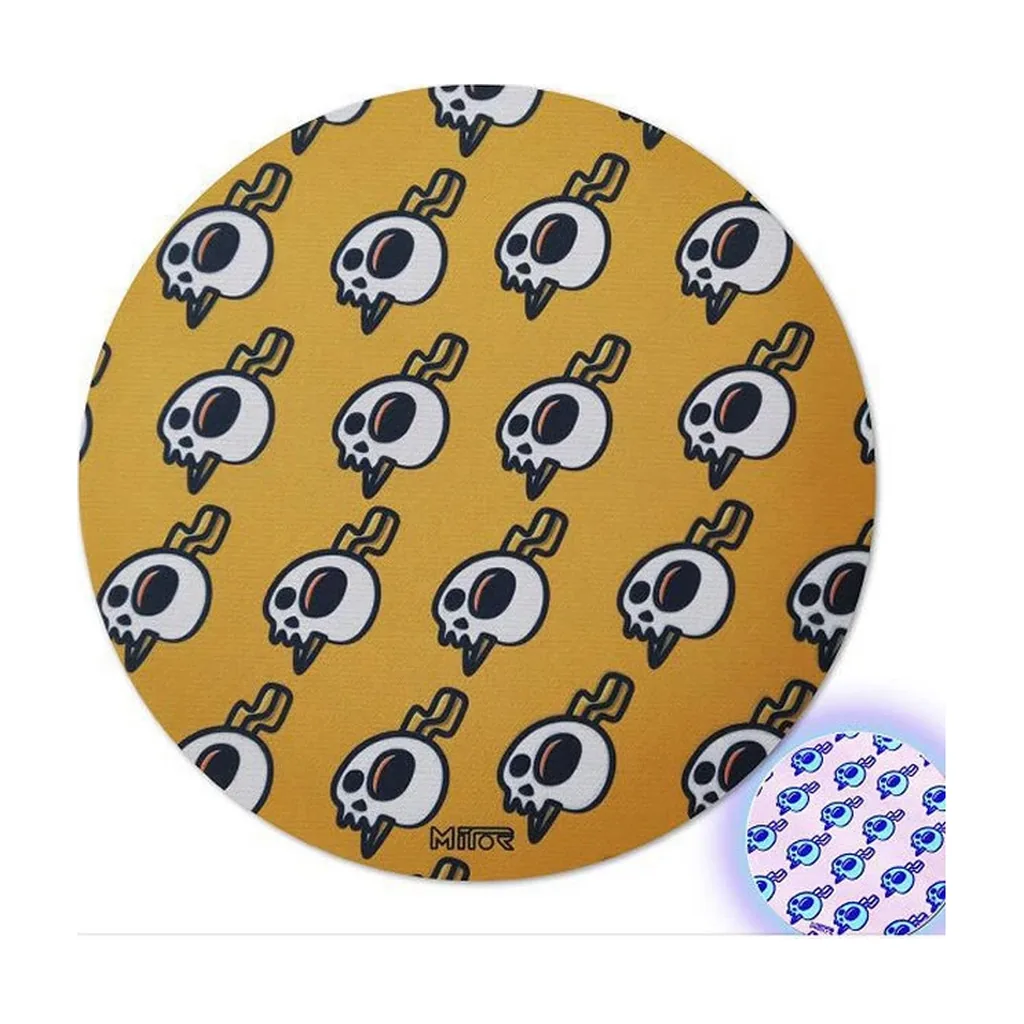 Tapete circular Mitor amarillo con un patrón de calaveras blancas y negras; un recuadro muestra el diseño en tonos azulados. Tapete circular Mitor amarillo con un patrón de calaveras blancas y negras; un recuadro muestra el diseño en tonos azulados.