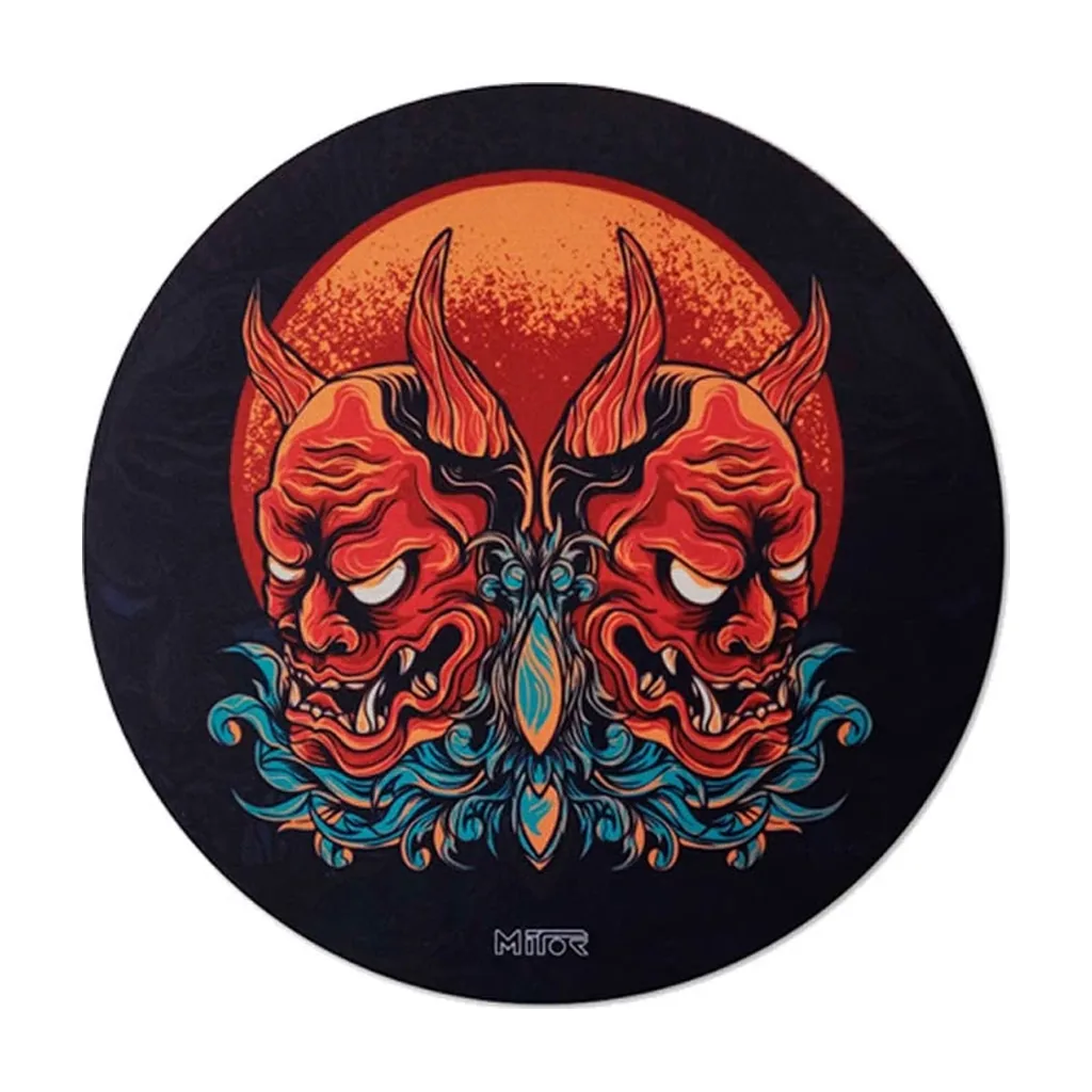 Tapete circular Mitor Hannya negro, decorado con máscaras rojas con cuernos, un círculo naranja y motivos ornamentales turquesa.