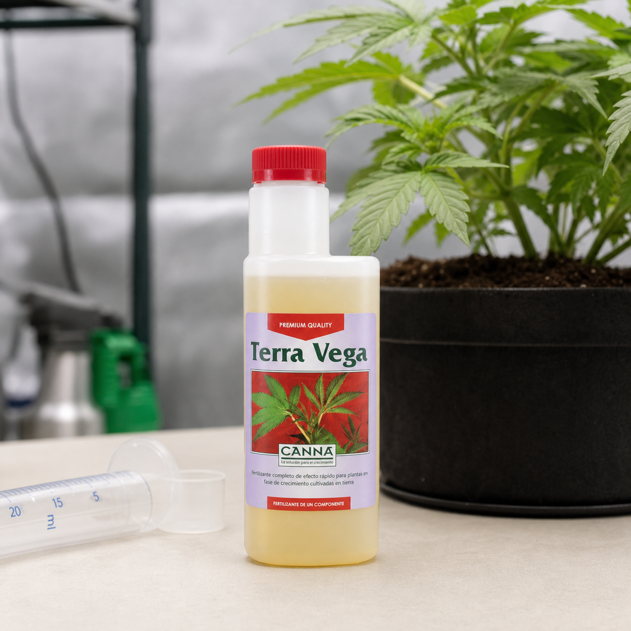 Botella de Canna Terra Vega con tapón rojo junto a una planta en maceta, una jeringa dosificadora y un vaso pequeño.