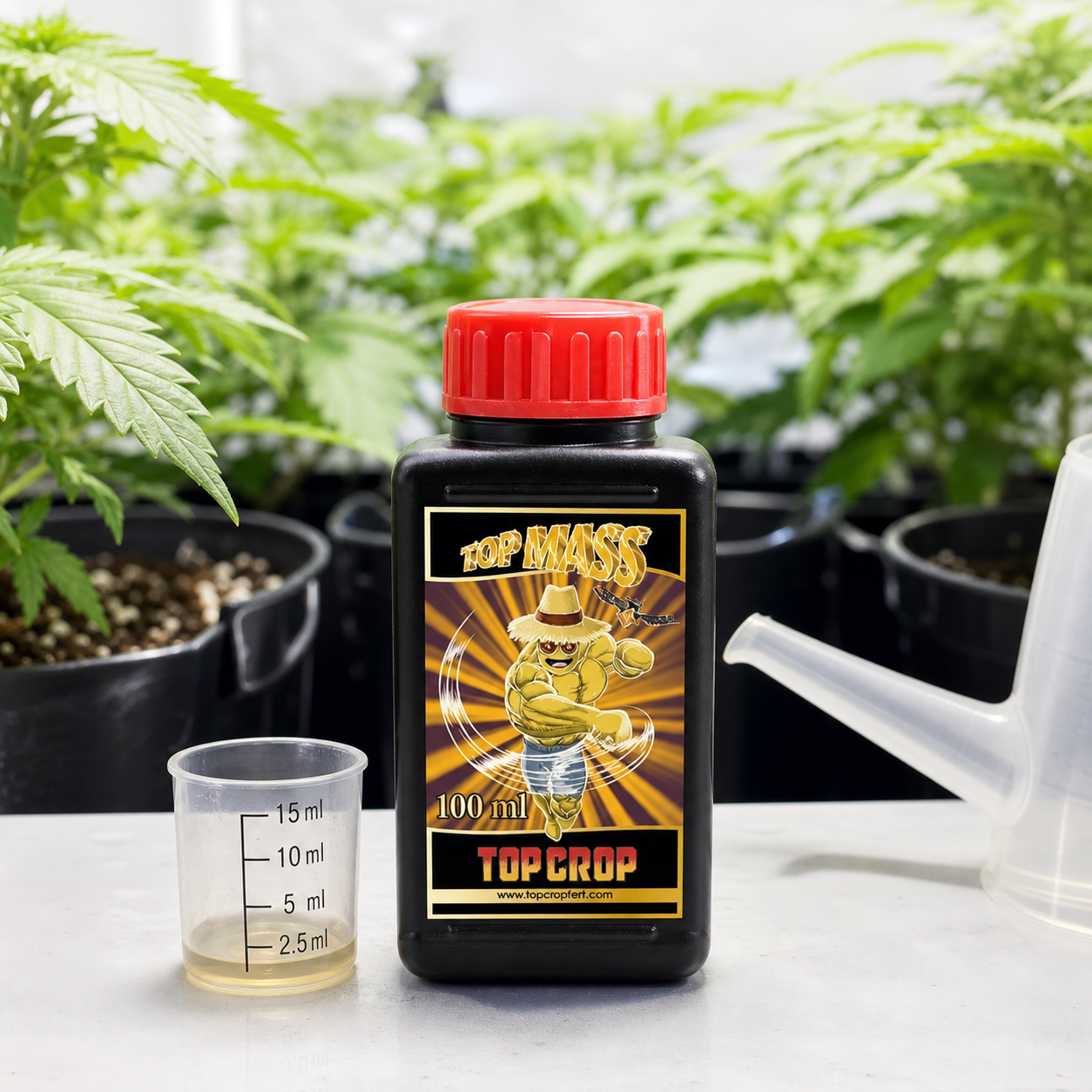 Botella de Top Mass Top Crop con tapón rojo, junto a un vaso graduado con líquido y una regadera, delante de plantas en macetas.