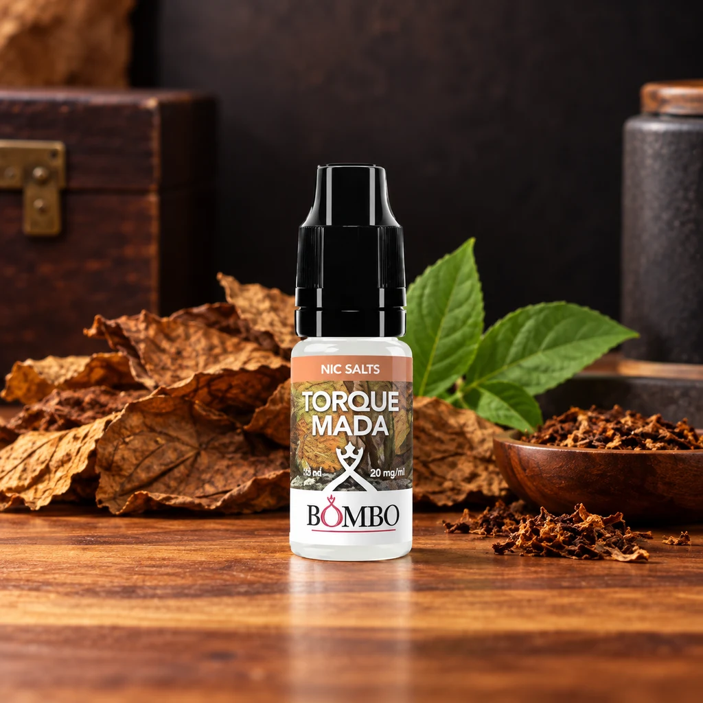 Frasco de Torquemada Bombo Nic Salts con tapón negro sobre una mesa de madera, rodeado de hojas secas, hojas verdes y tabaco picado.