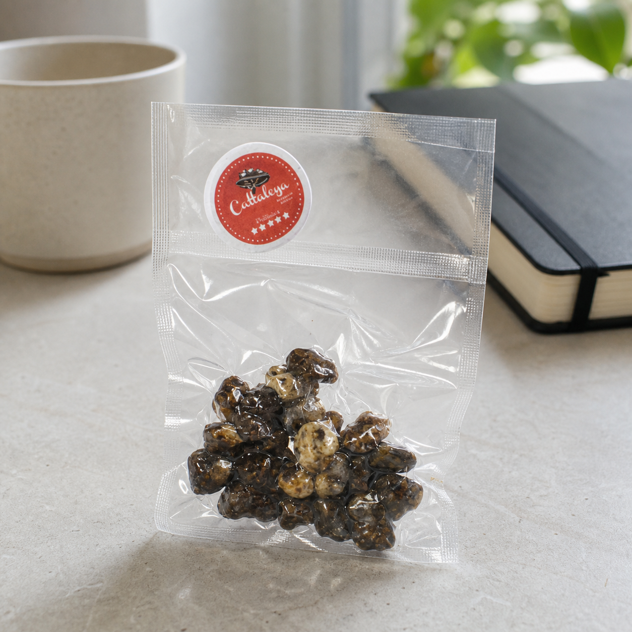Bolsa transparente de trufas Cattaleya con etiqueta circular roja, sobre una mesa junto a una taza y un cuaderno negro.