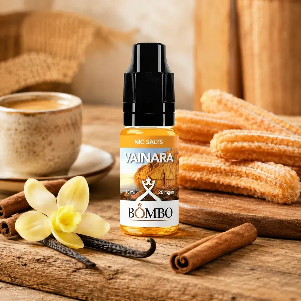 Frasco Vainara de Bombo con tapón negro y etiqueta de 10 ml y 20 mg/ml, junto a churros, una taza, vainilla y canela.