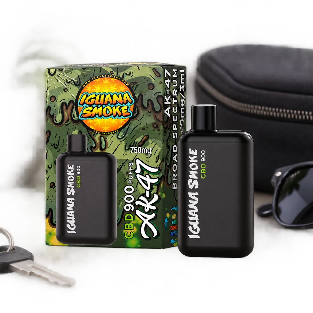 Vape negro Iguana Smoke junto a su caja verde rotulada AK-47, con un estuche, unas gafas y unas llaves sobre fondo oscuro.