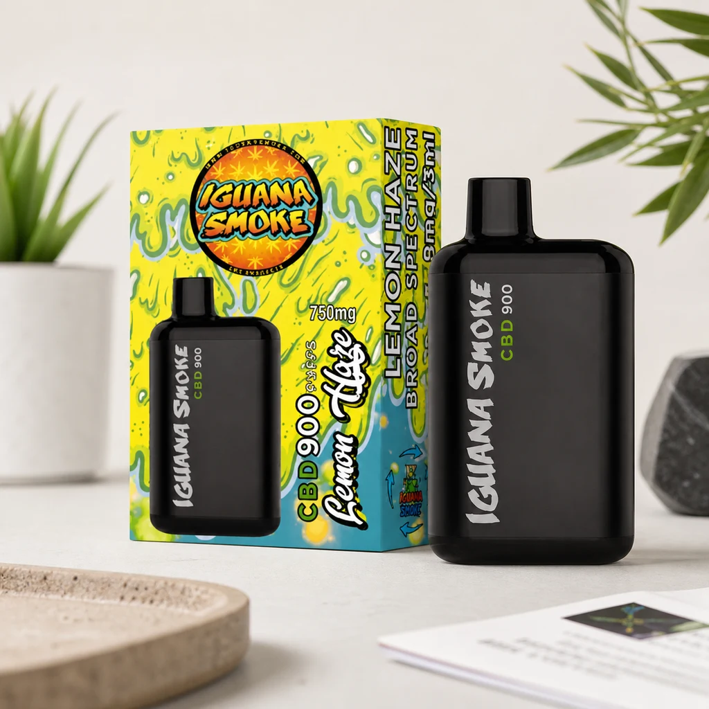 Vape negro Iguana Smoke CBD 900 junto a su caja amarilla y verde Lemon Haze, sobre una mesa clara con plantas al fondo.