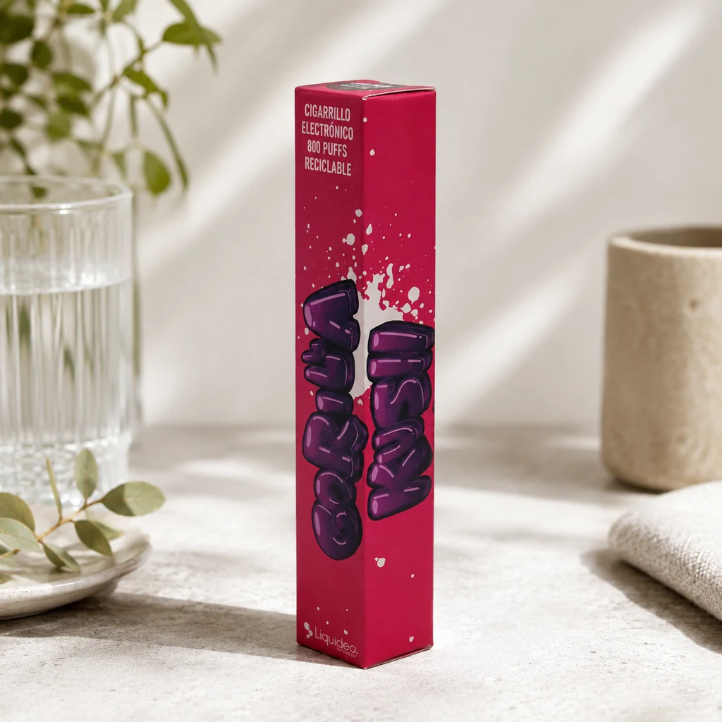 Caja fucsia de Wpuff Gorilla Kush de pie sobre una mesa, con el texto «800 puffs», junto a un vaso de agua y una toalla. Caja fucsia de Wpuff Gorilla Kush de pie sobre una mesa, con el texto «800 puffs», junto a un vaso de agua y una toalla.