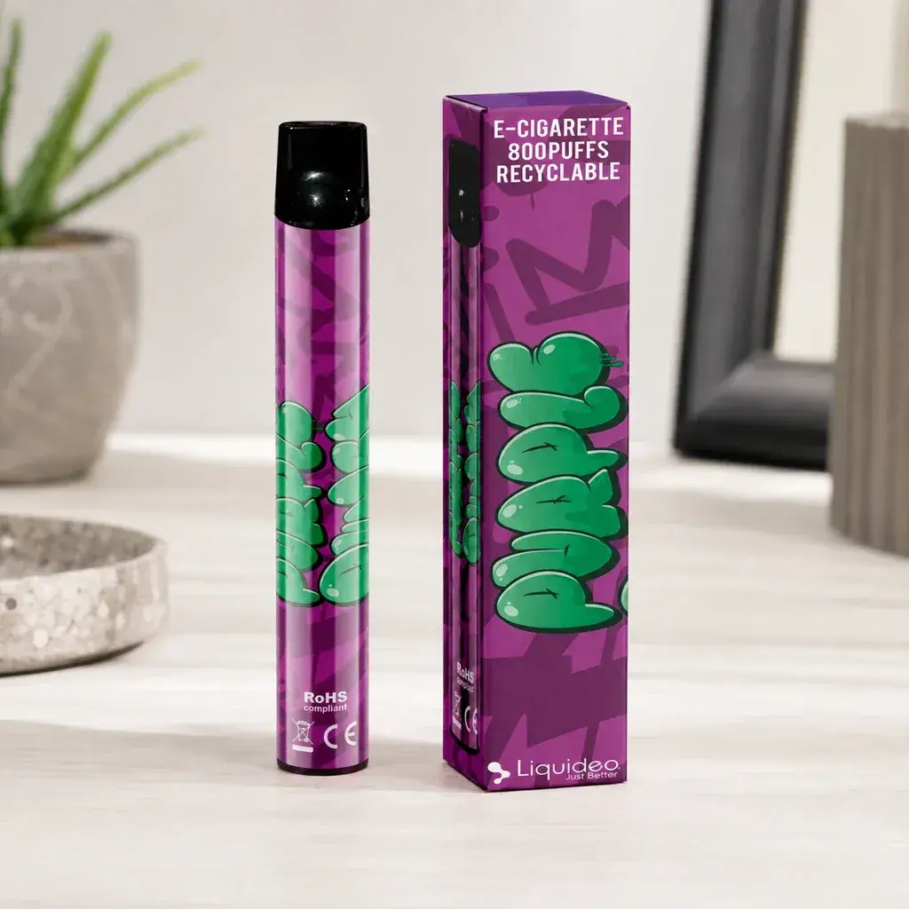 Escena generada de Wpuff Purple Punch de Liquideo: vaper morado con boquilla negra junto a su caja, sobre una mesa clara.