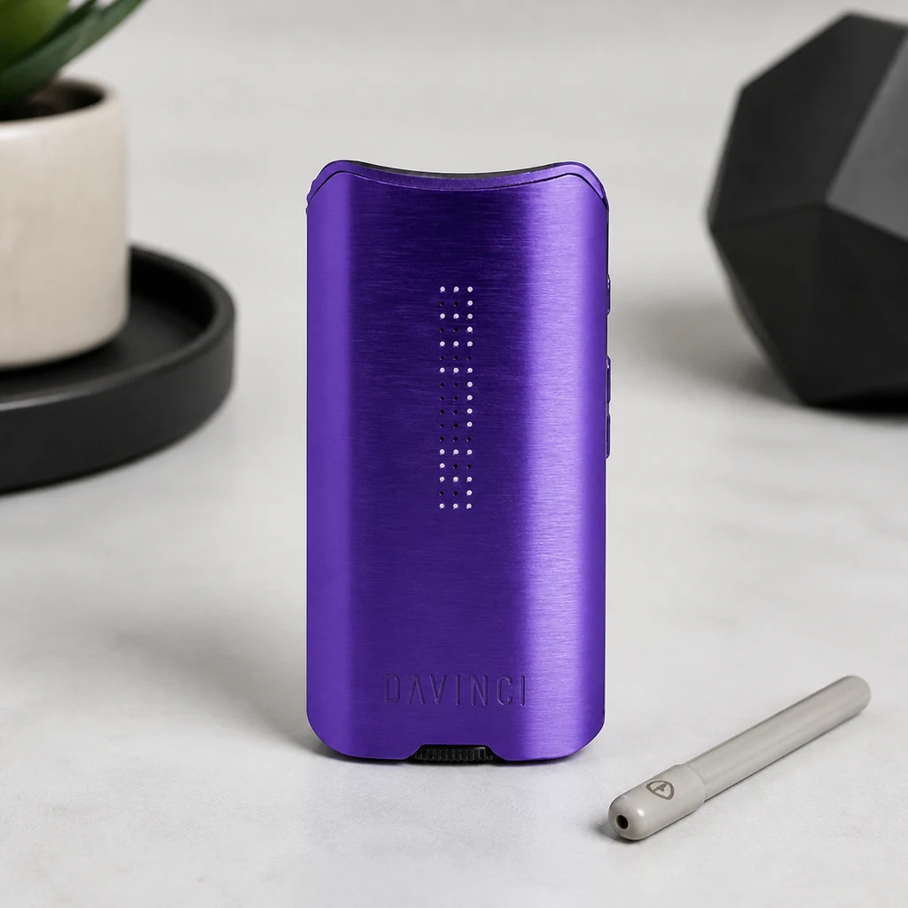 Vaporizador DaVinci IQ3 Amethyst morado, con puntos luminosos frontales y una pieza tubular a su lado sobre una superficie clara.