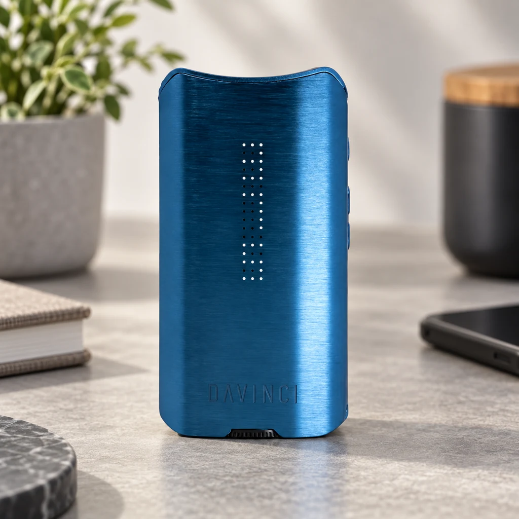 Vaporizador DaVinci IQ3 Sapphire azul sobre una encimera, con puntos luminosos frontales, una planta, libros y un móvil alrededor.