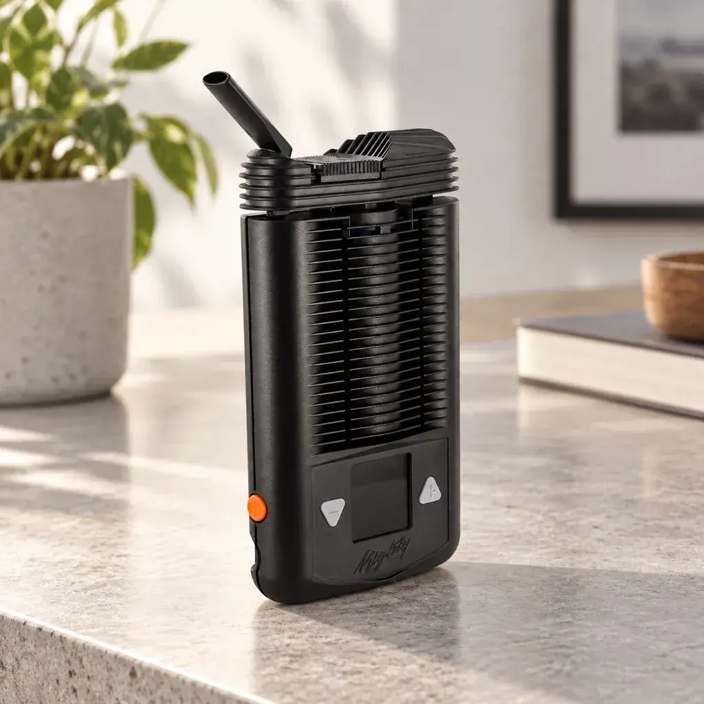 Vaporizador Mighty negro sobre una encimera, con boquilla inclinada, cuerpo acanalado, pantalla frontal y botón lateral naranja.