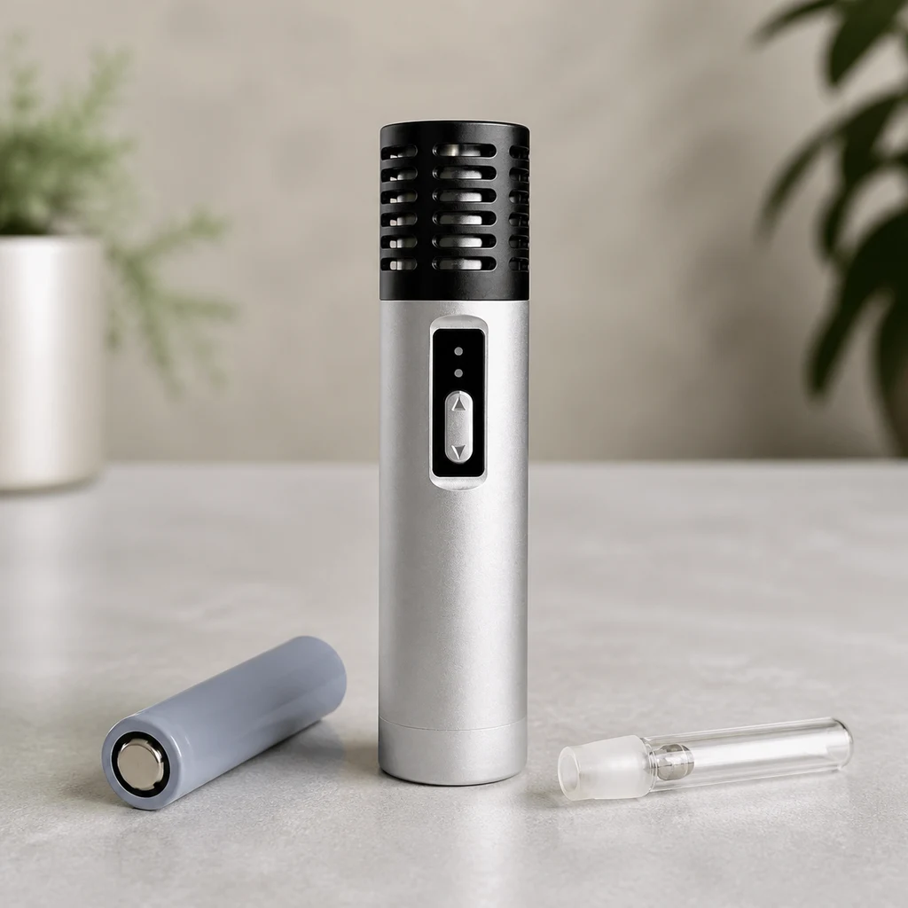 Vaporizador Arizer Air Silver de pie, con cuerpo plateado, rejilla negra y control frontal, junto a una batería y una boquilla transparente.