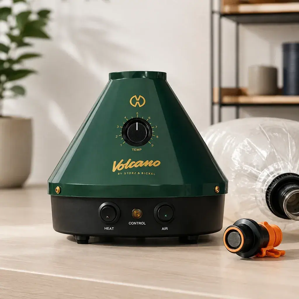 Volcano Classic 25 Year Edition verde con base negra, dial frontal y botones, junto a un globo transparente y una pieza naranja y negra.