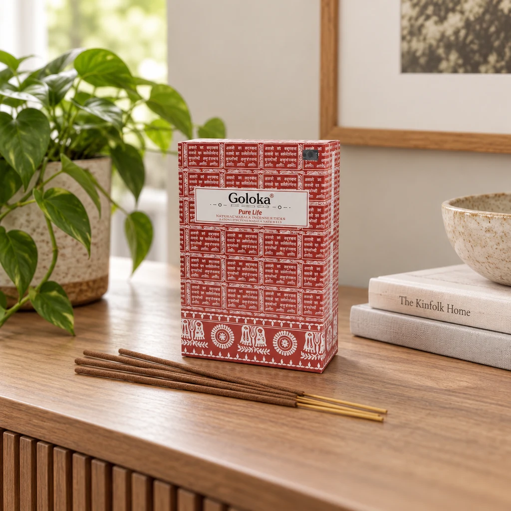 Caja roja estampada de incienso Goloka Pure Life con varias varillas sobre un mueble de madera, junto a una planta y libros.
