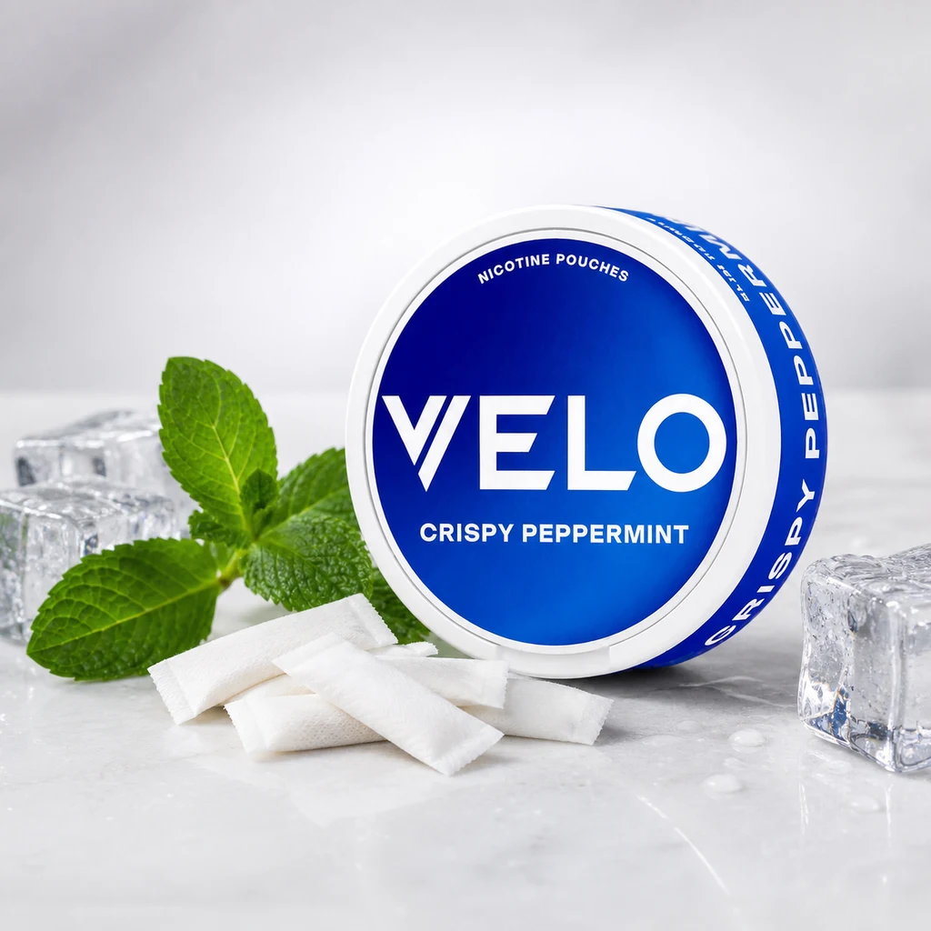 Envase redondo azul y blanco de VELO Crispy Peppermint junto a bolsas blancas, hojas de menta y cubitos de hielo.