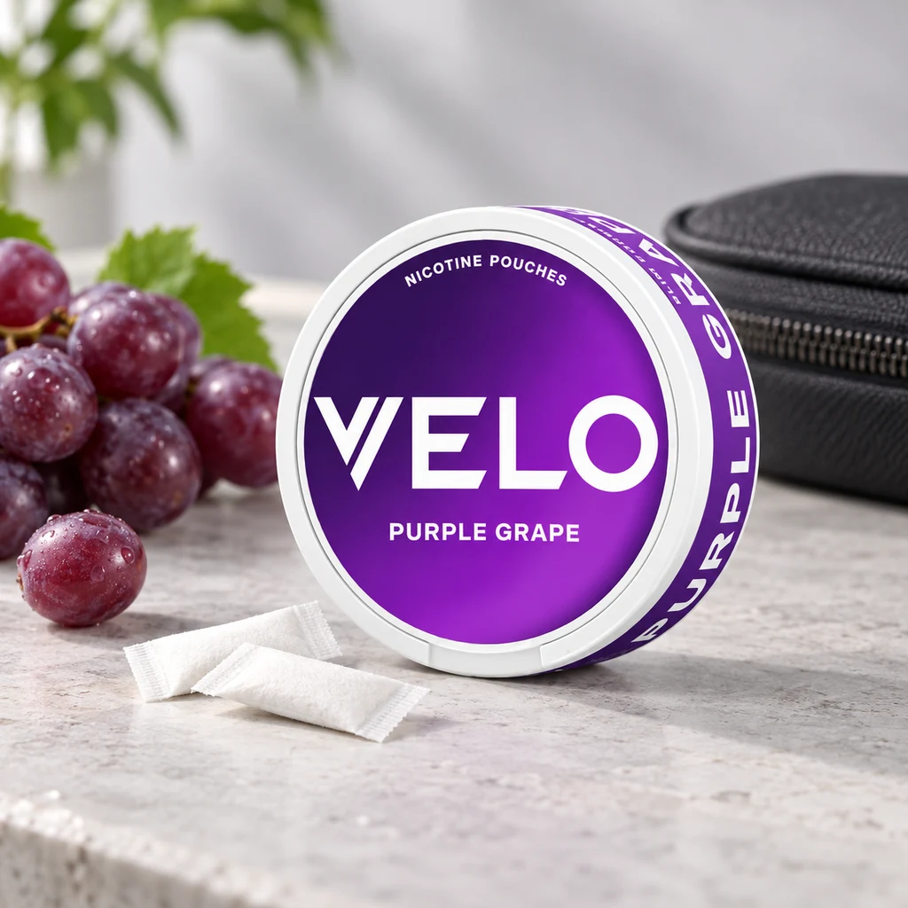 Envase redondo VELO con etiqueta morada «Purple Grape», junto a bolsitas blancas, uvas y un estuche negro. Envase redondo VELO con etiqueta morada «Purple Grape», junto a bolsitas blancas, uvas y un estuche negro.
