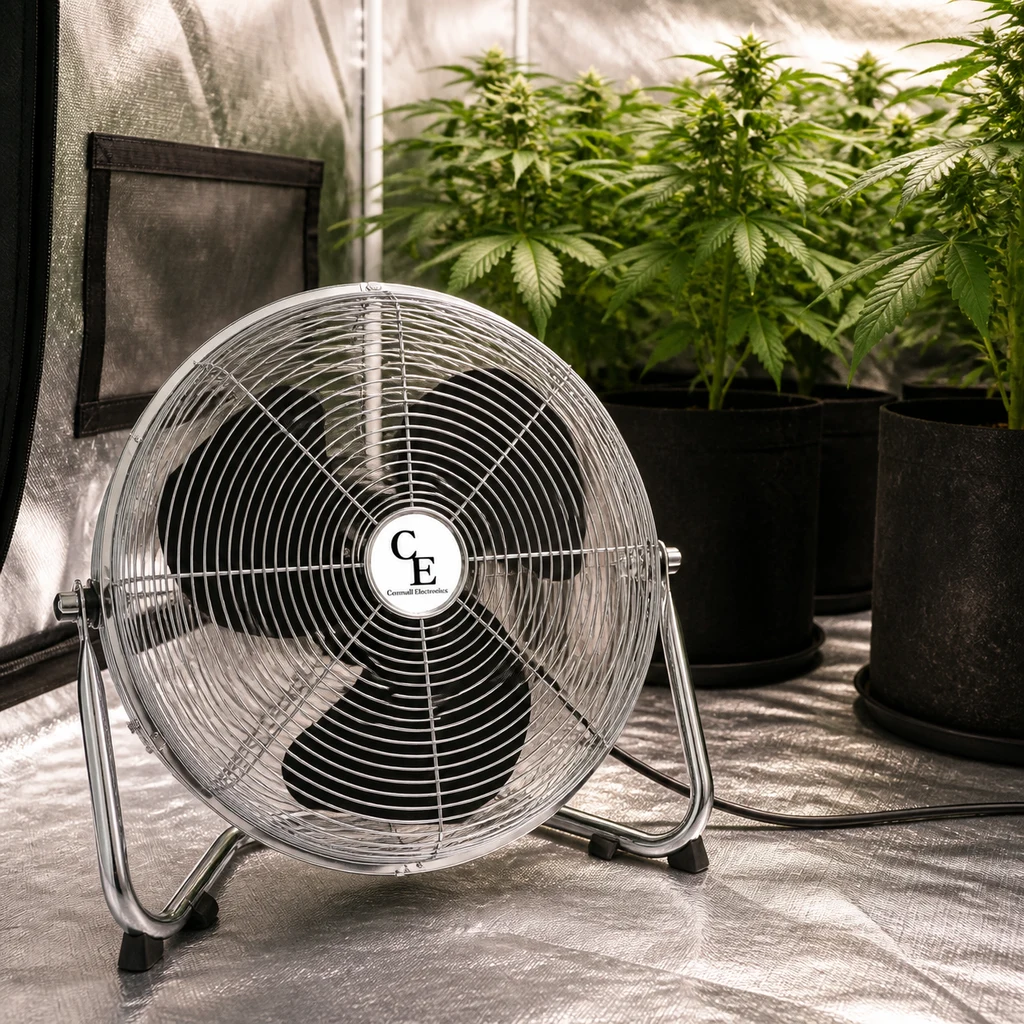 Ventilador Cornwall Electronics con rejilla plateada, aspas negras y soporte de suelo, frente a plantas en un armario de cultivo.