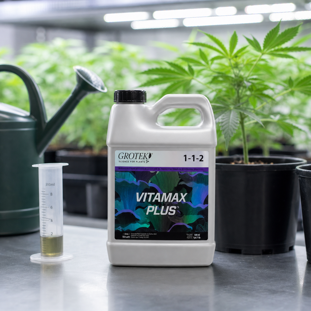 Envase blanco de Vitamax Plus Grotek con asa y tapón negro, junto a una probeta con líquido y una regadera, delante de plantas. Envase blanco de Vitamax Plus Grotek con asa y tapón negro, junto a una probeta con líquido y una regadera, delante de plantas.