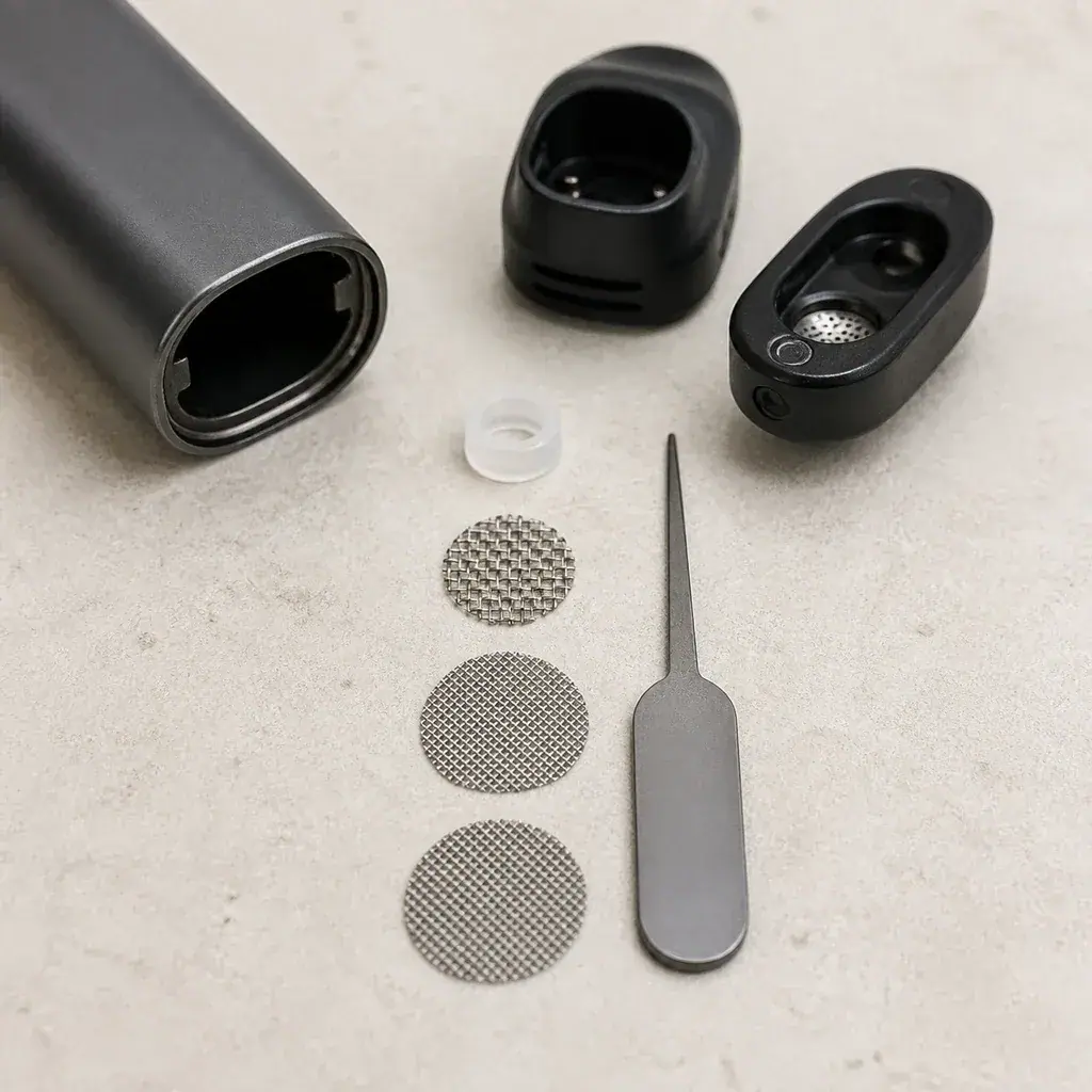 Filtros circulares de malla del X-max V3 Nano junto a piezas de un vaporizador desmontado, un aro translúcido y una herramienta metálica.